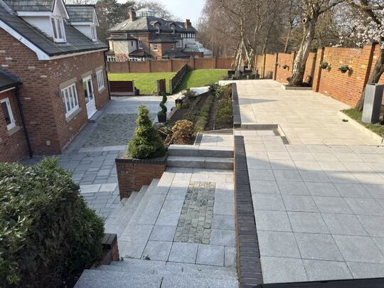 After: large tiered back garden with a paved terrace, steps and paths beside a brick house