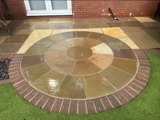 After: stone circle patio with a brick border, next to artificial grass